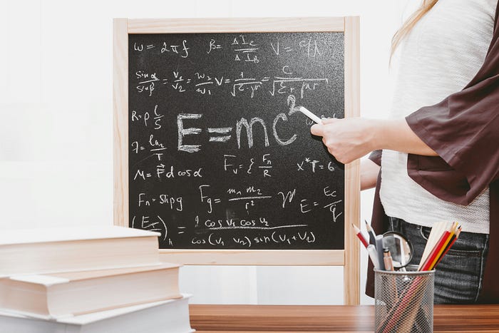 Person writing mathematical equations on a chalkboard – physics and education concept with Einstein’s E=mc² formula.
