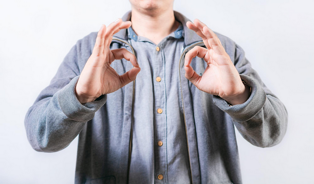 Person making an ‘OK’ hand gesture – body language and nonverbal communication concept with a casual outfit.