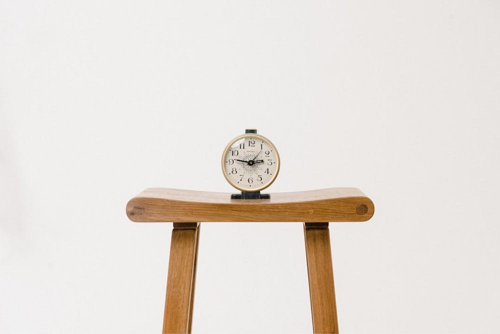 Minimalist wooden stool with a vintage clock – simple and aesthetic time management concept in a clean, white space.