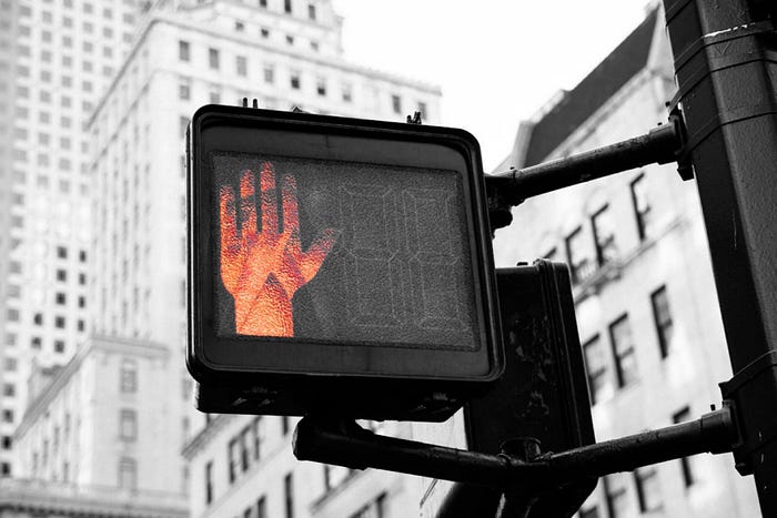 Urban crosswalk signal with a glowing red stop hand – city street safety sign with skyscrapers in the background.
