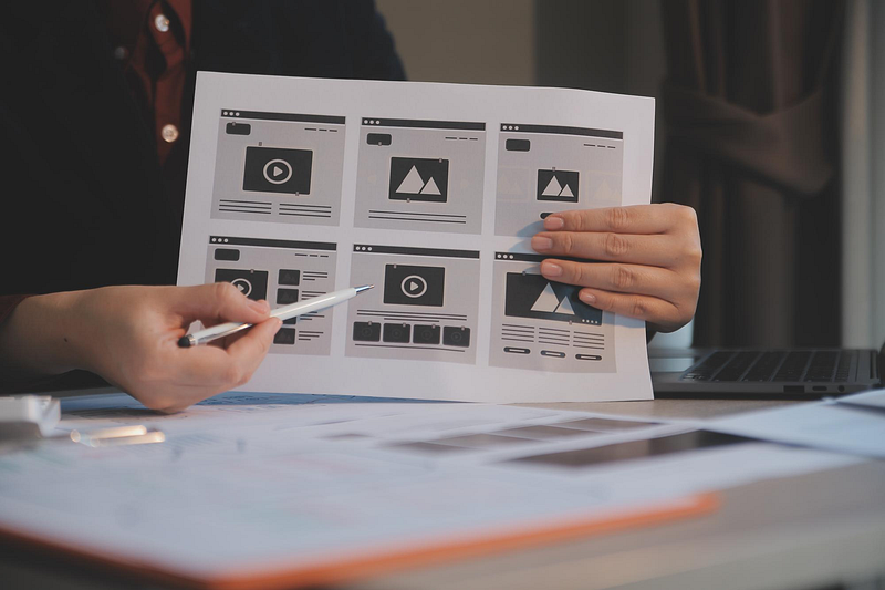 Designer reviewing website wireframes on paper – UX and UI design planning process for a digital project.