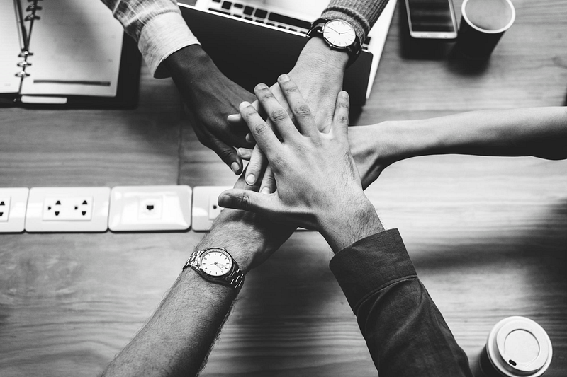 Black and white photo of hands stacked together – teamwork, unity, and corporate success concept.